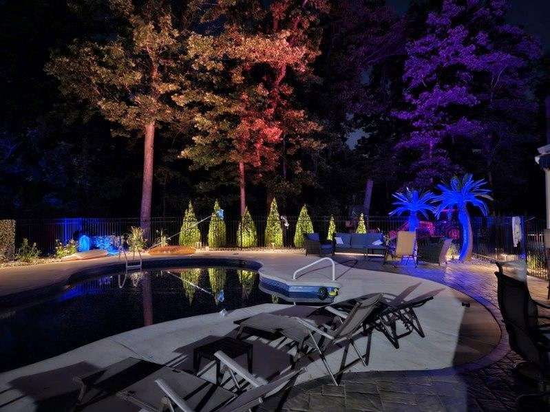 Pool ringed by trees uplit in red, blue and purple
