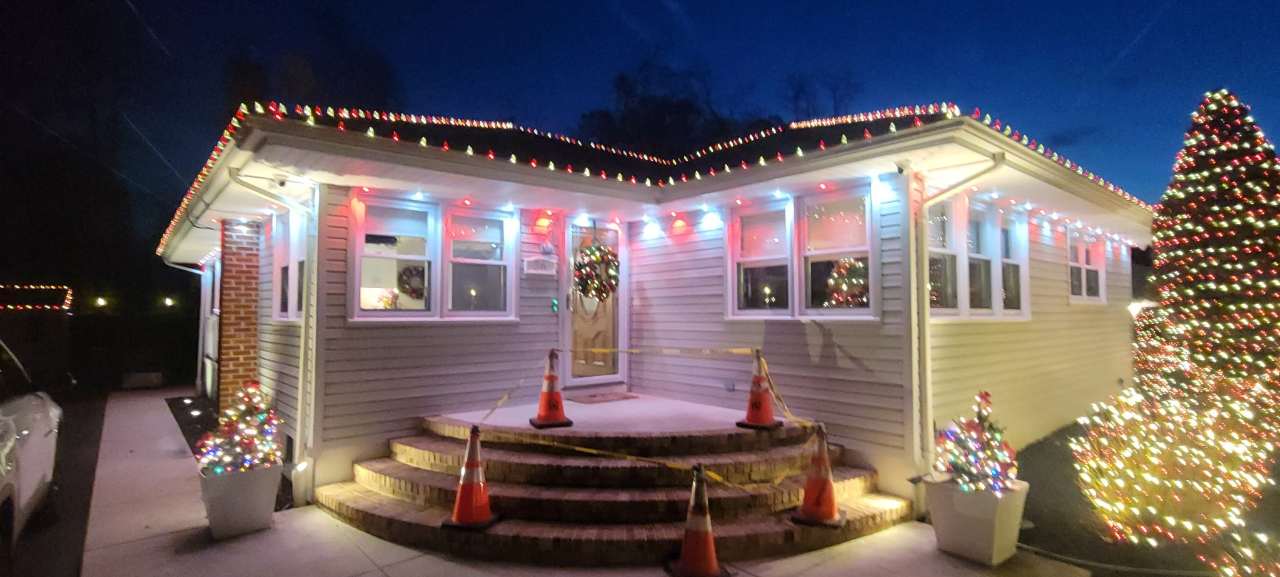 Home outlined in holiday lights with lit trees