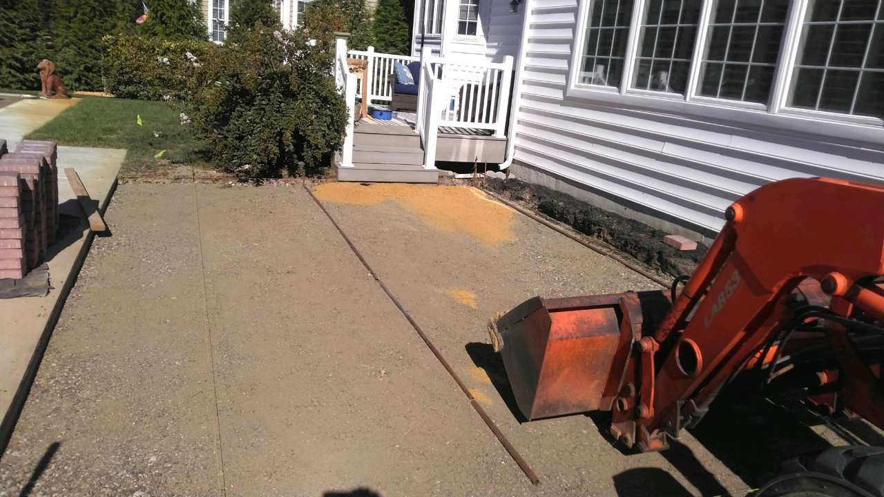 Compacted base, stacked pavers and an excavator before the patio install