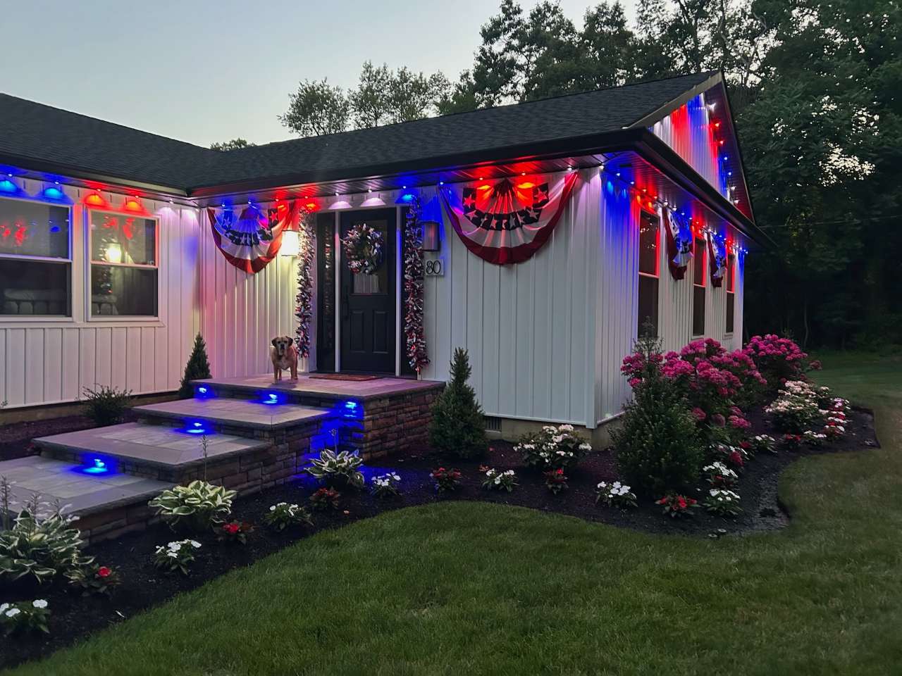 Front porch and beds lit with red, white and blue accent lighting at dusk